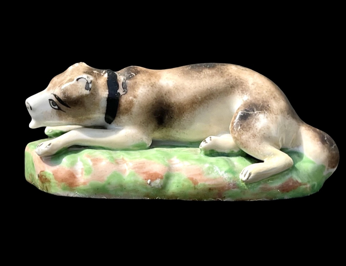 Sculpture en porcelaine polychrome représentant un chien couché dans l'herbe. Jacob Petit