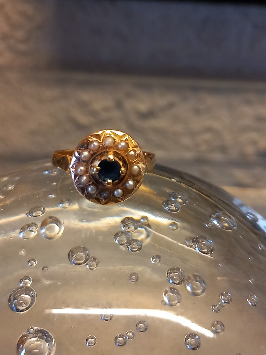 Bague circulaire en or 18k, au centre un saphir entouré d'un rang de demi perles.