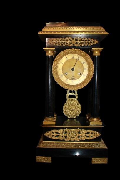 French Clock From The Mid-1800s In Empire Style, Ebonized Wood, With Rich Bronze Applications. 