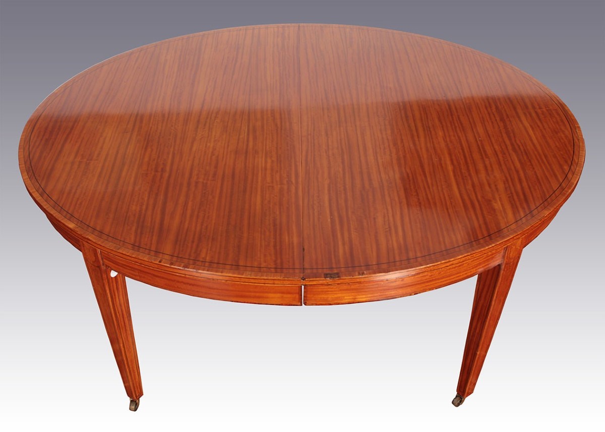 Extendable Oval Table In Satin Wood With Inverted Pyramid Legs That Rest On Metal Wheels