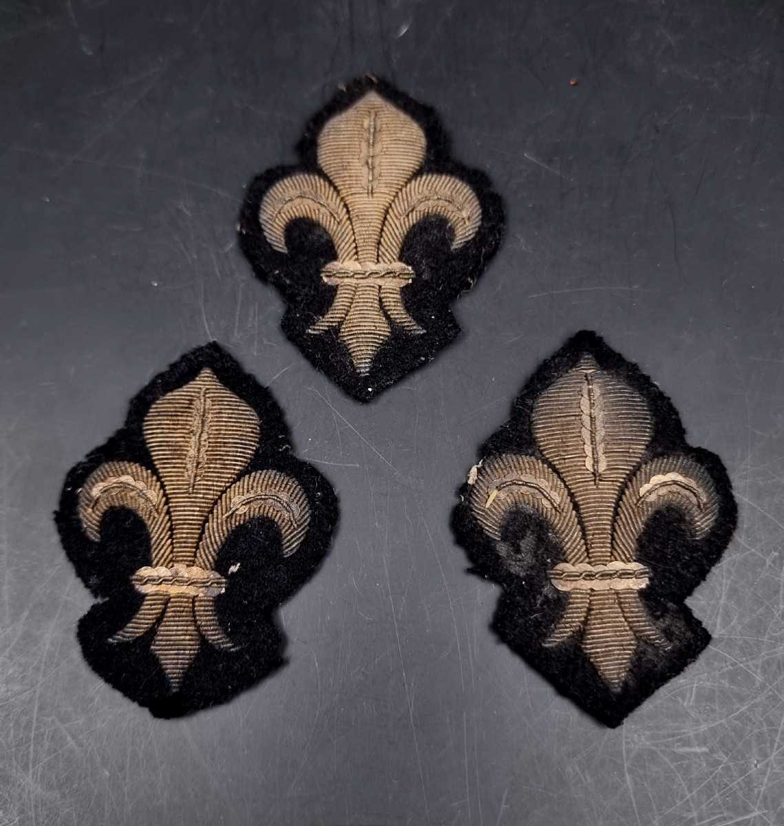 Three Fleur-de-lys Embroidered In Gold Thread On A Black Background