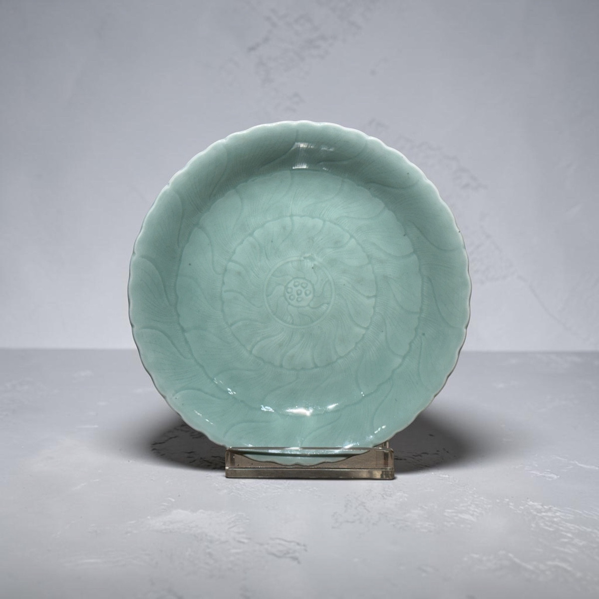 ASSIETTE EN CÉLADON, bord ondulé et décor en relief composé de cercles concentriques formant qu