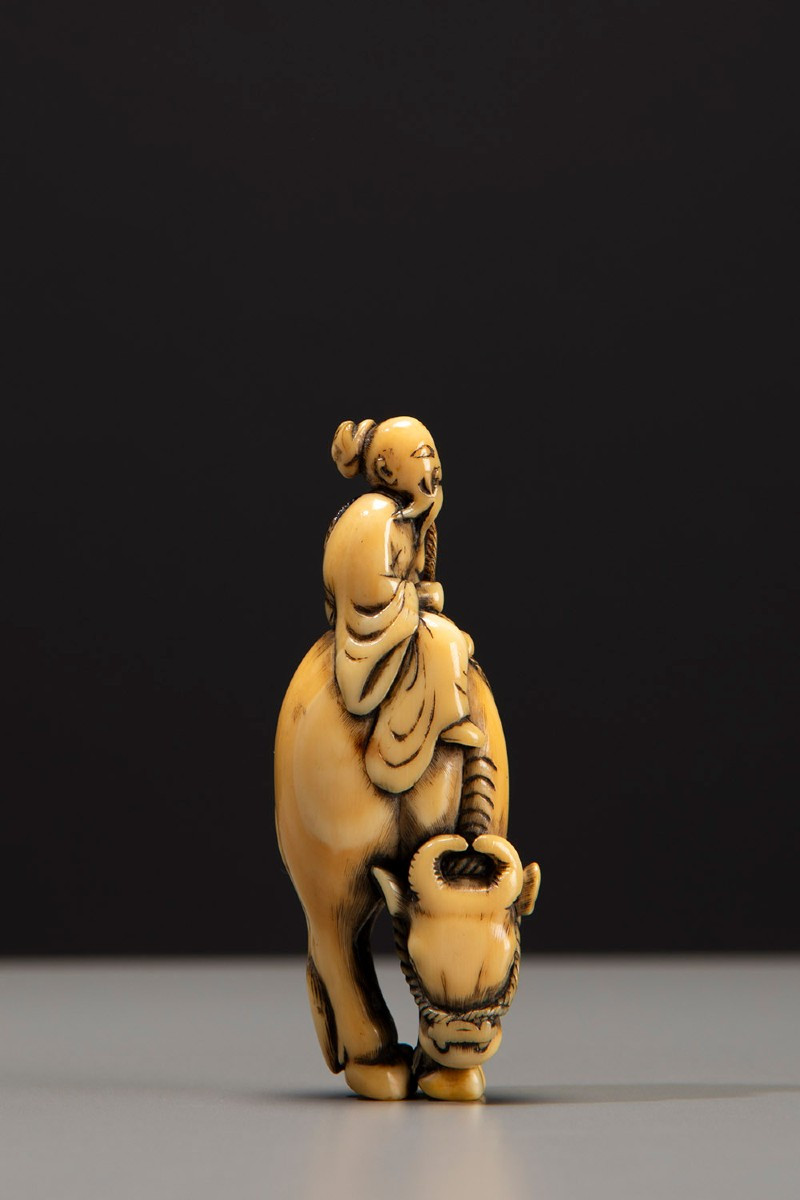 An Ivory Netsuke Depicting Roshi Seated On The Back Of A Buffalo