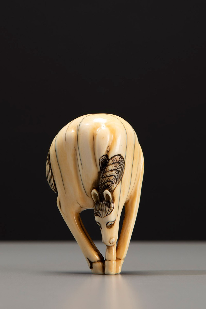 An Ivory Netsuke Depicting A Horse With Lowered Head And Joined Legs