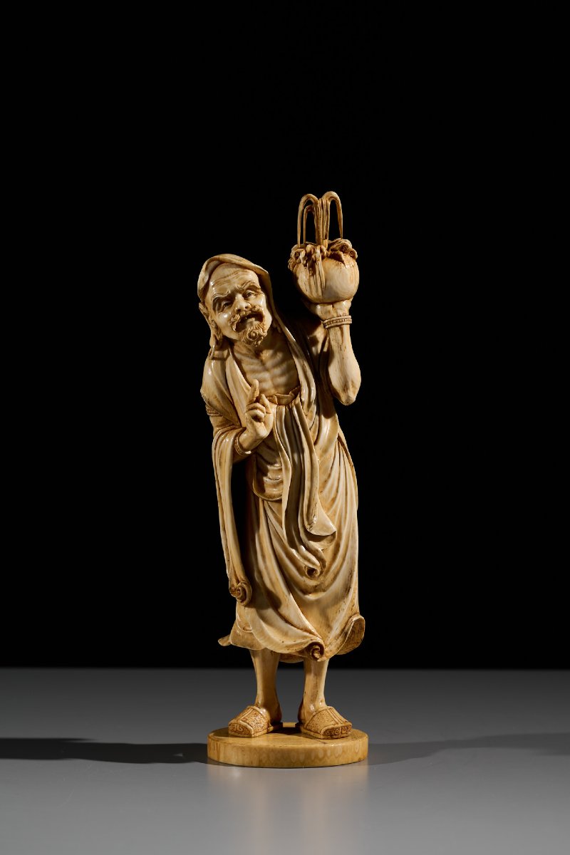 An Ivory Okimono Of A Rakan Holding A Ritual Vase, Signed Kazutoshi