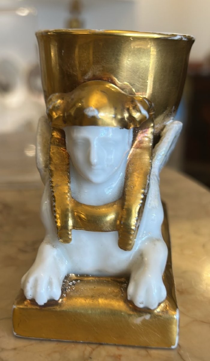 Encrier en porcelaine à corps blanc et rehauts d'or, reposant sur un sphinx égyptien.