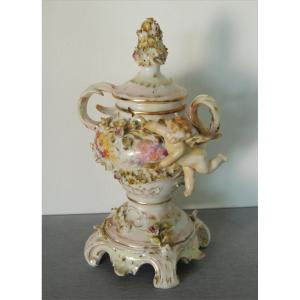 Biscuit Porcelain, Covered Pot Decorated With Slip And Flowers Supporting An Angel 