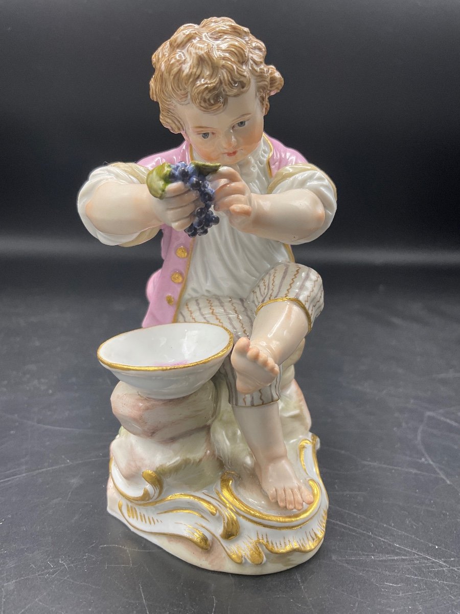 Porcelaine De La Manufacture De Meissen Polychrome Représentant Un Jeune Garçon Assis Pressant une grappe de raisin dans un bol.
