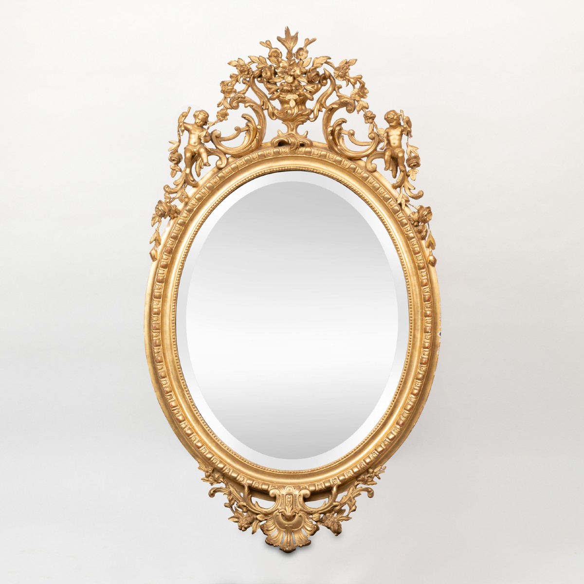 Miroir ovale en bois et stuc doré à fronton aux putti, XIXe