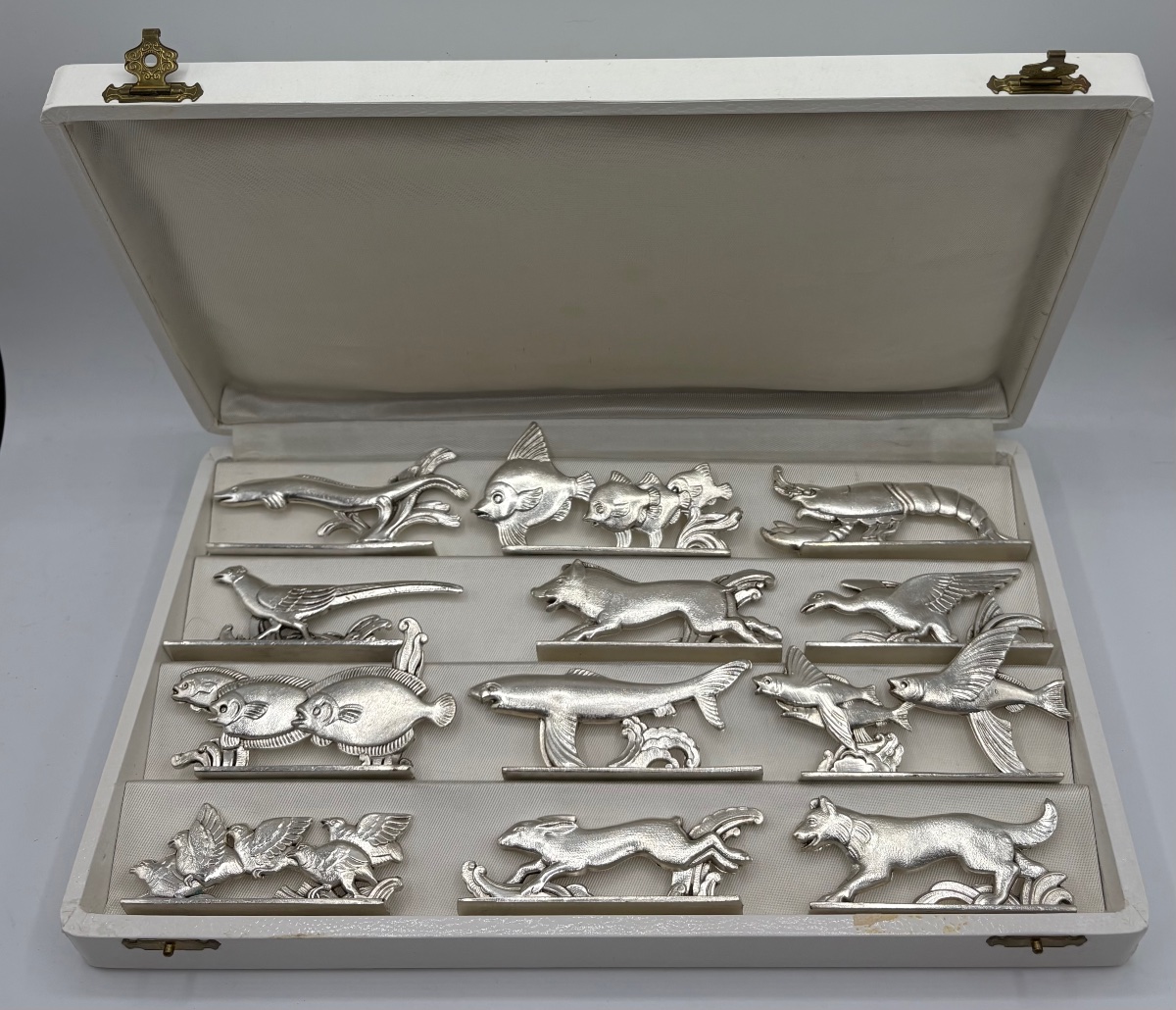 UN COFFRET DE DOUZE PORTES COUTEAUX DES ANNÉES 1930 EN MÉTAL ARGENTÉ DE CHEZ ORBRILLE