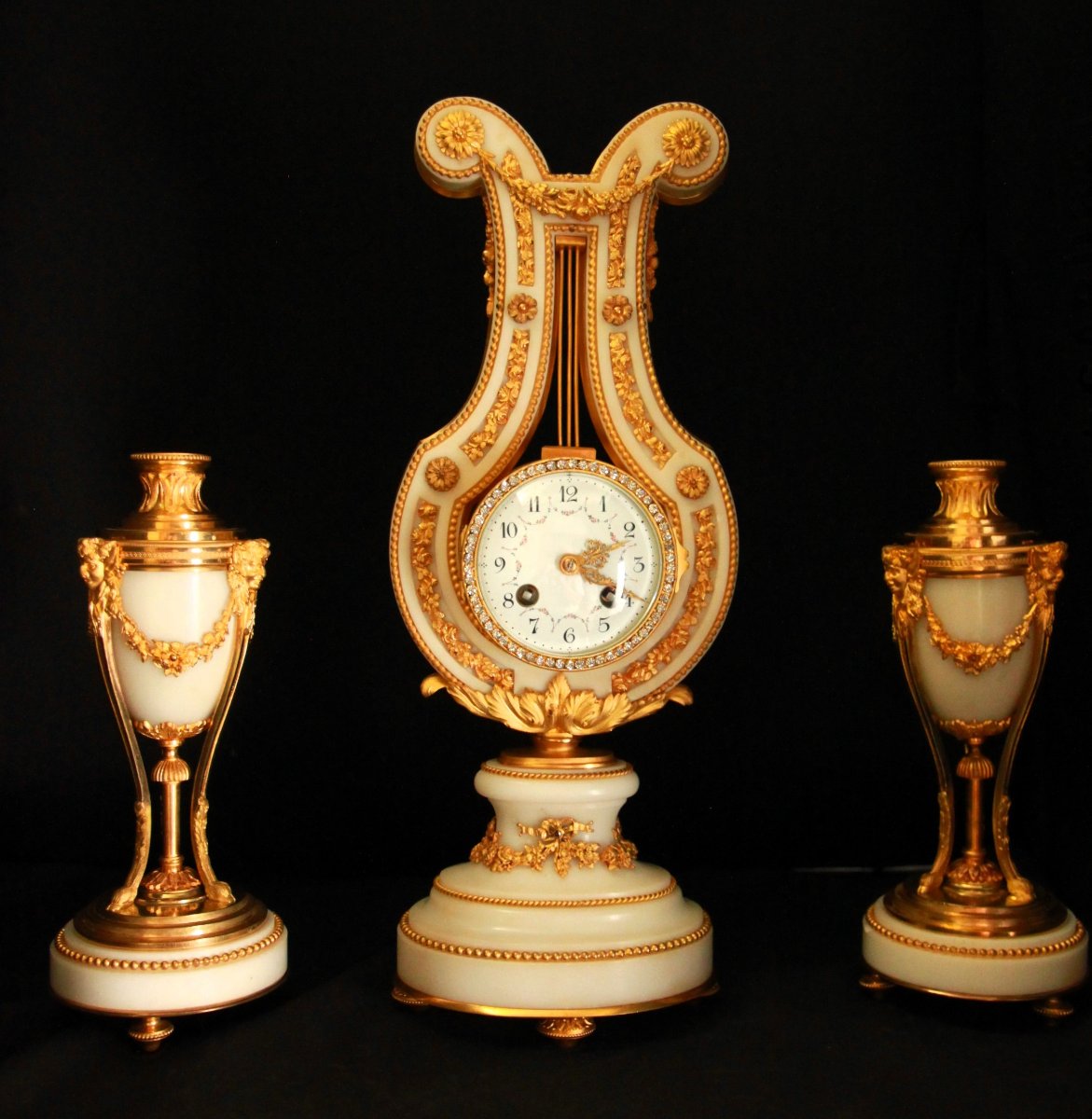 Pendule de cheminée de style lyre accompagnée de deux candélabres assortis.